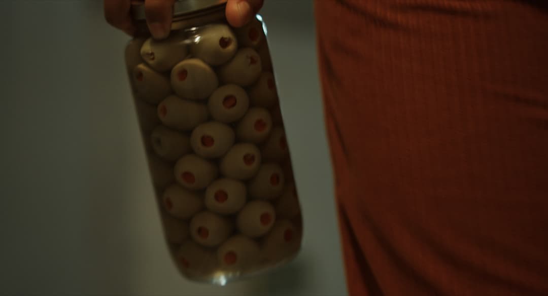 A close-up shot of a jar of olives in someone's hand