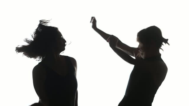 Two silhoutted dancers in front of a plain white backdrop