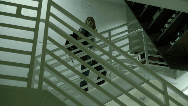 Kate climbs a dark industrial staircase