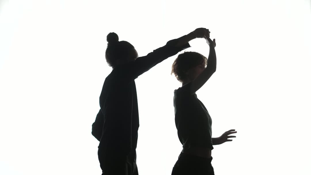 Two silhoutted dancers in front of a plain white backdrop