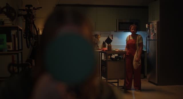 A woman looks at a person in the foreground, who stares into a mirror