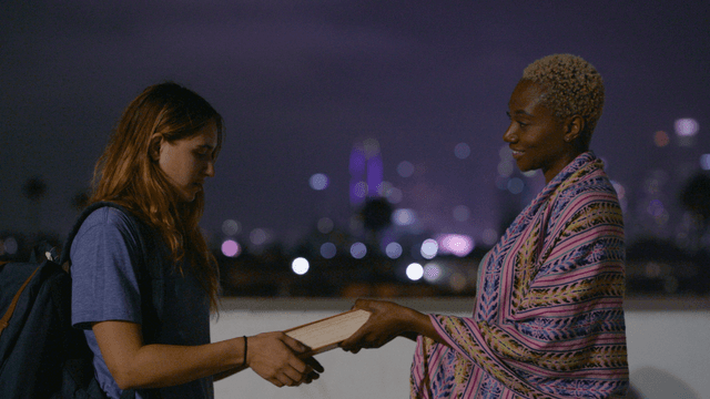 Helena hands Kate a book with the LA skyline in the background