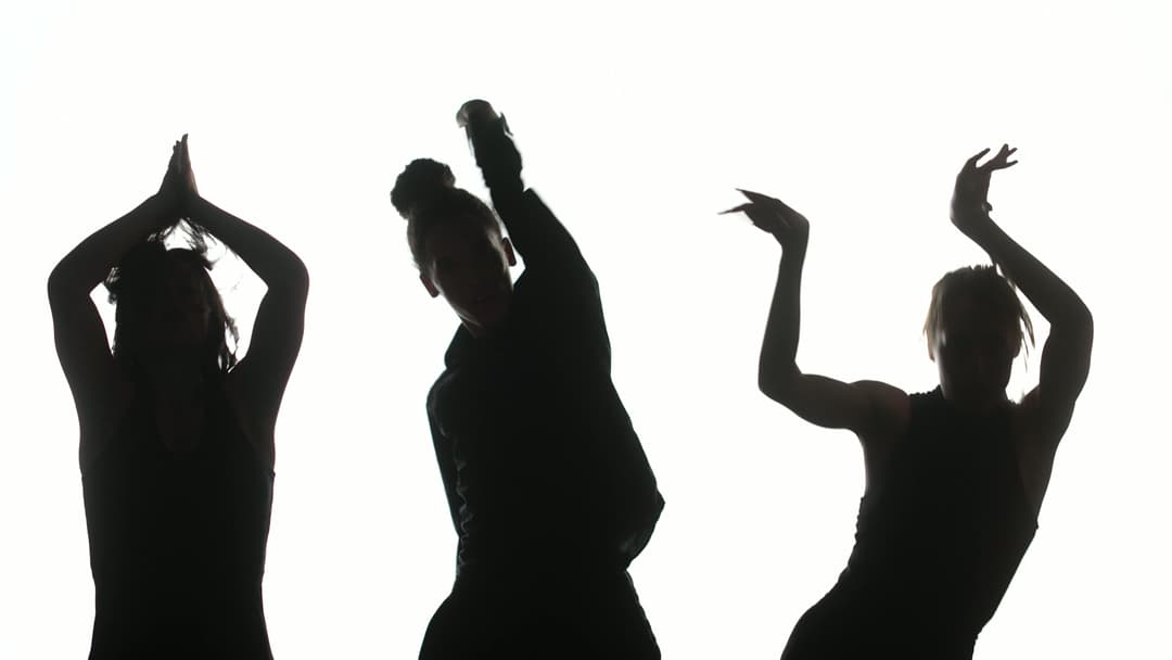 Three silhoutted dancers in front of a plain white backdrop