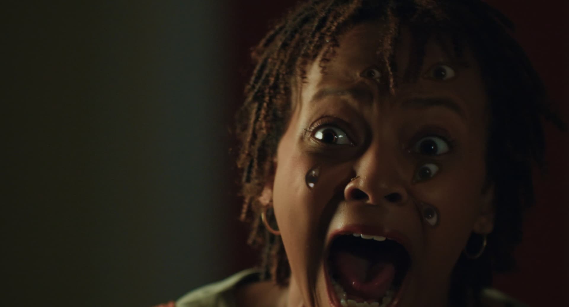 A woman with eyeballs all over her face, looking in the mirror and screaming