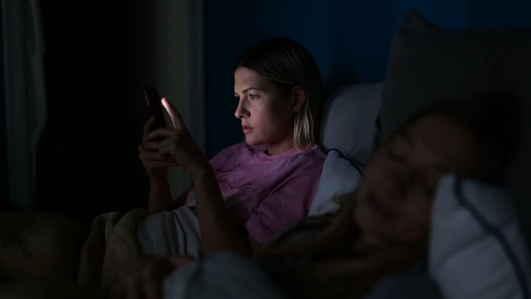 Two women in bed, one on her phone and one asleep