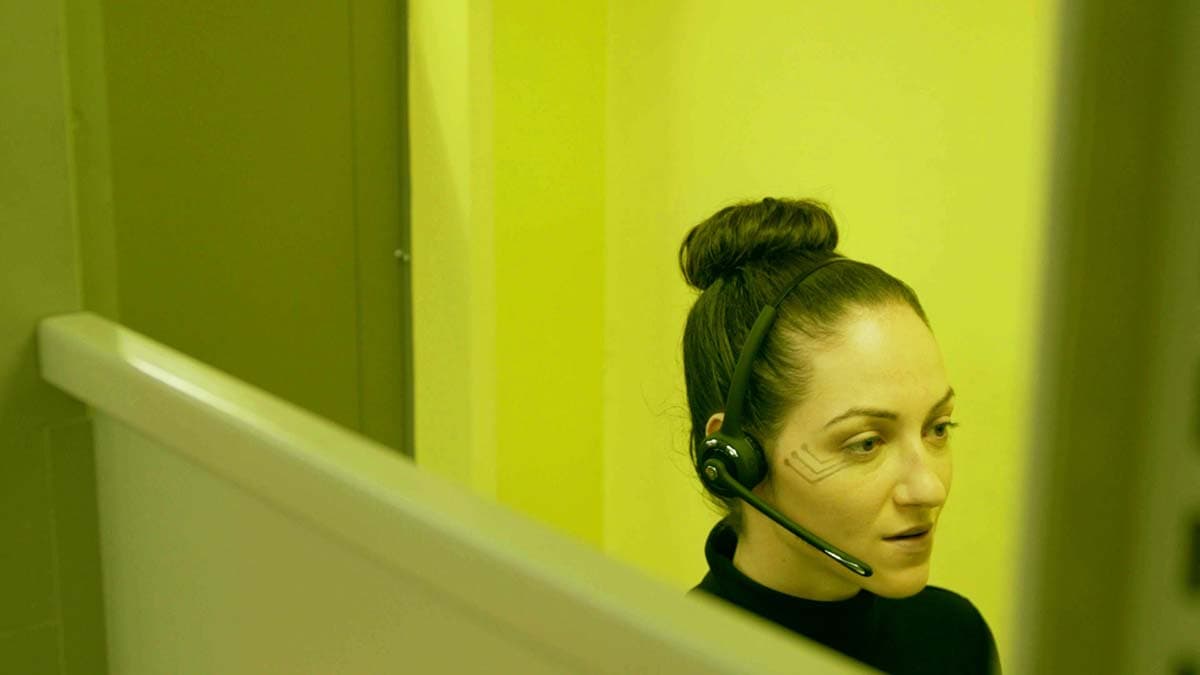 An android sits at her cubicle, talking on the phone via a headset.