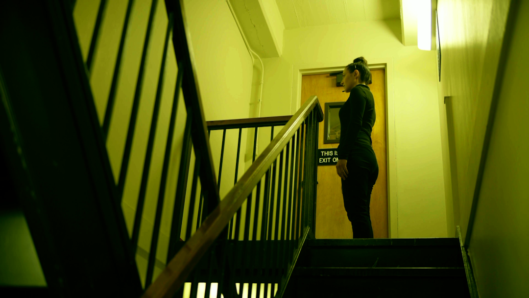 Jone stands by herself at a staircase landing